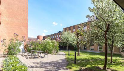 Orange tegelbyggnad med träd i förgrunden. Boplatsgatan 8